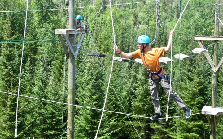a student wearing safety gear makes their way over an obstacle in a high ropes course
